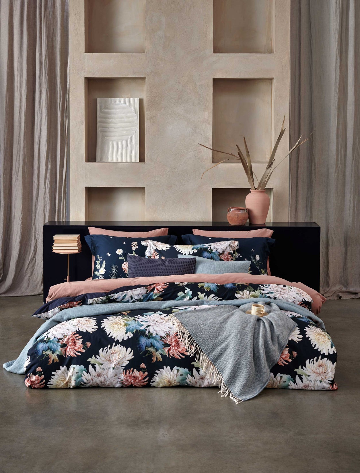 een bed in een rustige, serene omgeving met een bed met een dekbedovertrek in donkerblauw met daarop bloemen geprint, een dekbedovertrek in een roze kleur en een sprei van wol en katoen in een blauwe kleur