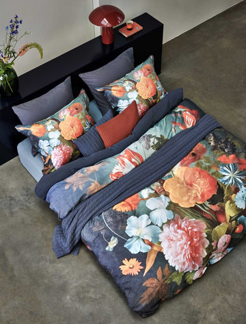 Een topshot van een bed met een dekbedovertrek met bloemen print in oranje en blauwe kleuren