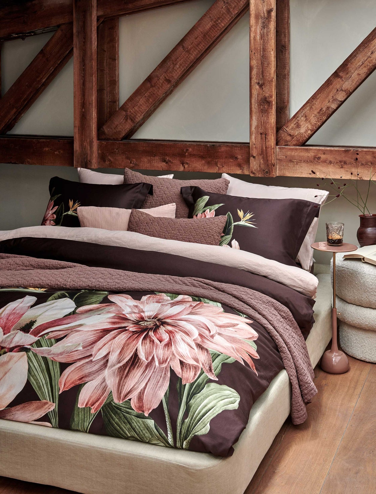 Een bed met een dekbedovertrek in een bruine kleur met een grote roze bloem en een sprei en sierkussens in een bruine kleur