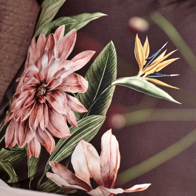 detail shot van een bruin hoofdkussen met een roze bloem en groene bladeren en een paradijsvogel