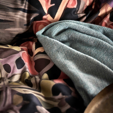 detail shot van een plaid van wol mix in een blauwe kleur en een dekbedovertrek met print in paarse en oranje kleuren