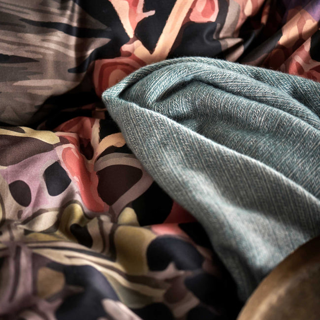 detail shot van een plaid van wol mix in een blauwe kleur en een dekbedovertrek met print in paarse en oranje kleuren