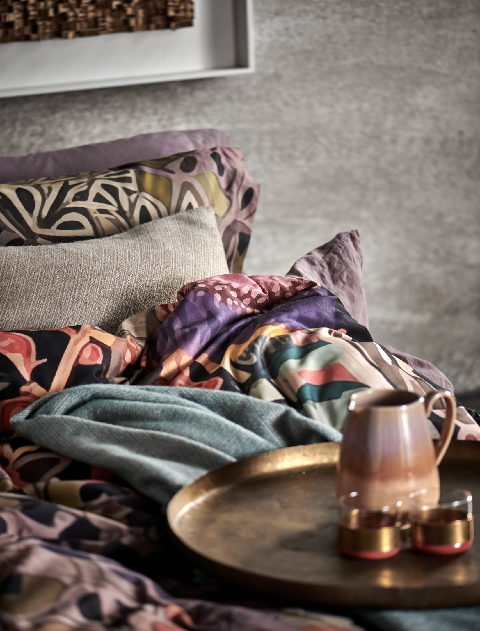 detail shot van een bed met een dekbedovertrek met print en een sierkussen in een beige kleur en een koffiekan met twee kopjes