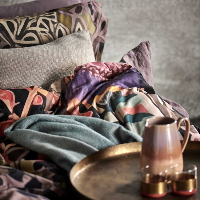 detail shot van een bed met een dekbedovertrek met print en een sierkussen in een beige kleur en een koffiekan met twee kopjes