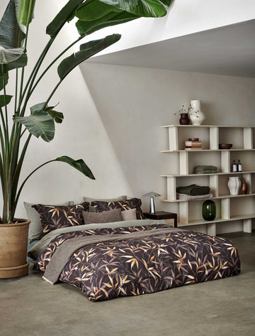 bed in een rustige omgeving met een monstera plant op het bed ligt een bruin dekbedovertrek met bamboe takken