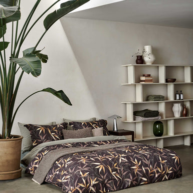 bed in een rustige omgeving met een monstera plant op het bed ligt een bruin dekbedovertrek met bamboe takken