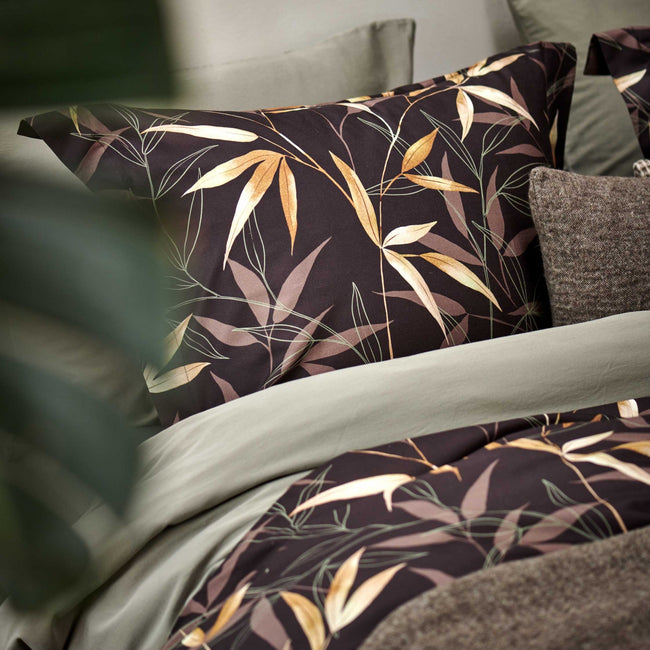 detail shot van een bed met een bruin dekbedovertrek met bamboe takken en een groen/thyme dekbedovertrek 
