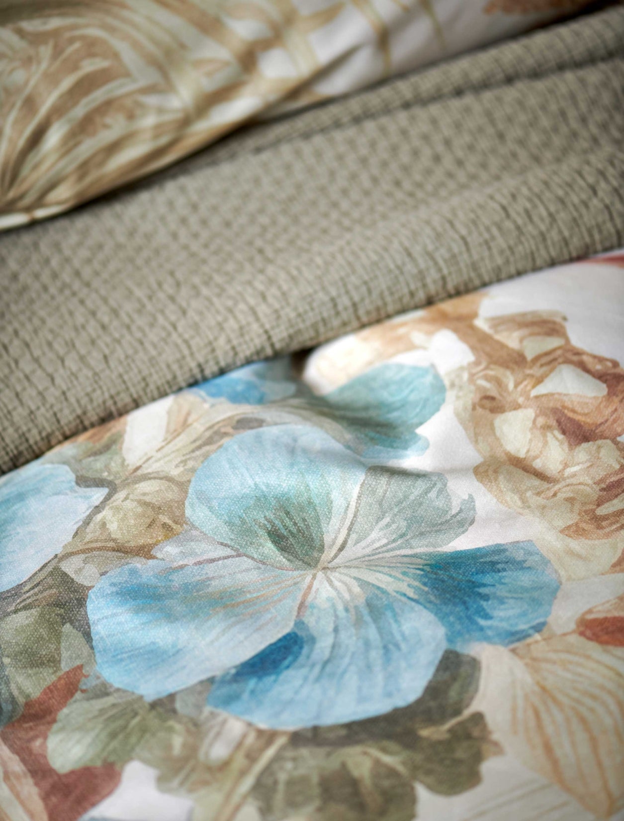 Florentine multi dekbedovertrek heeft enorme bloemen en bladeren in rood, blauw, oranje, groen en bruine tinten op een off white achtergrond, waarbij de tinten een soort sepia gloed lijken te hebben. De achterkant van het dekbedovertrek is effen beige.