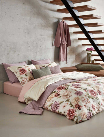 HARMONY dekbedovertrekset | cream tan Een bed in een rustige setting met een dekbedovertrek met rode, paarse en beige bloemen. Op het bed ligt een sprei in een lila kleur en in een groene kleur