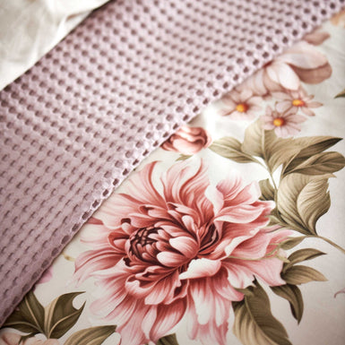 detail shot van een dekbedovertrek in een beige kleur met roze bloemen en een wafelsprei in een lila kleur