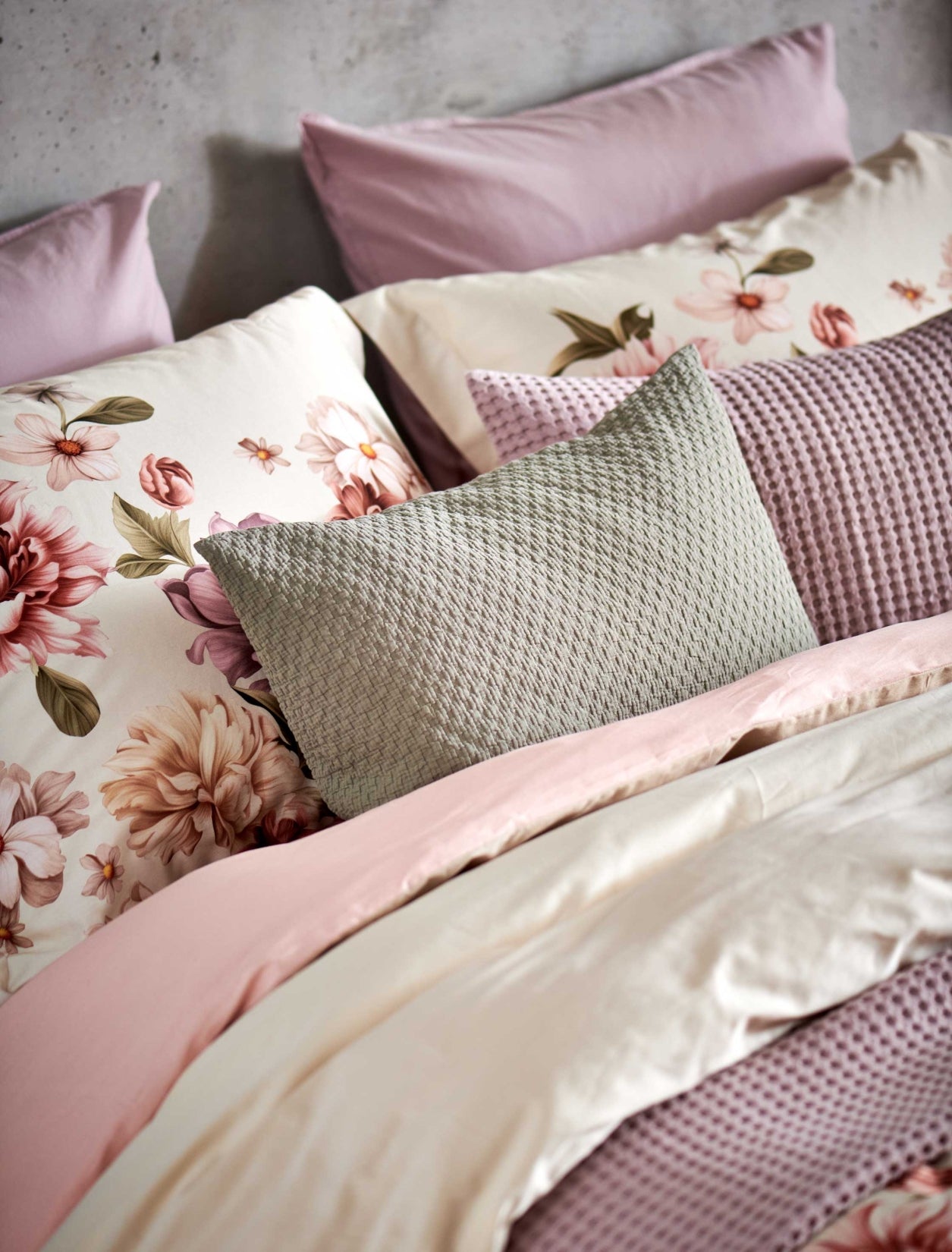 detail shot van een bed met een beige dekbedovertrek met roze en beige bloemen en sierkussens in lila en groene kleuren