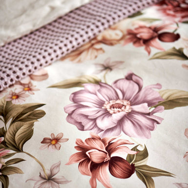 detail shot van een dekbedovertrek in een beige kleur met roze en paarse bloemen met groene bladeren