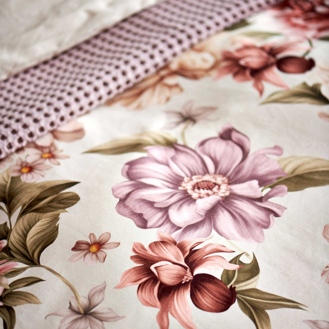 detail shot van een dekbedovertrek in een beige kleur met roze en paarse bloemen met groene bladeren