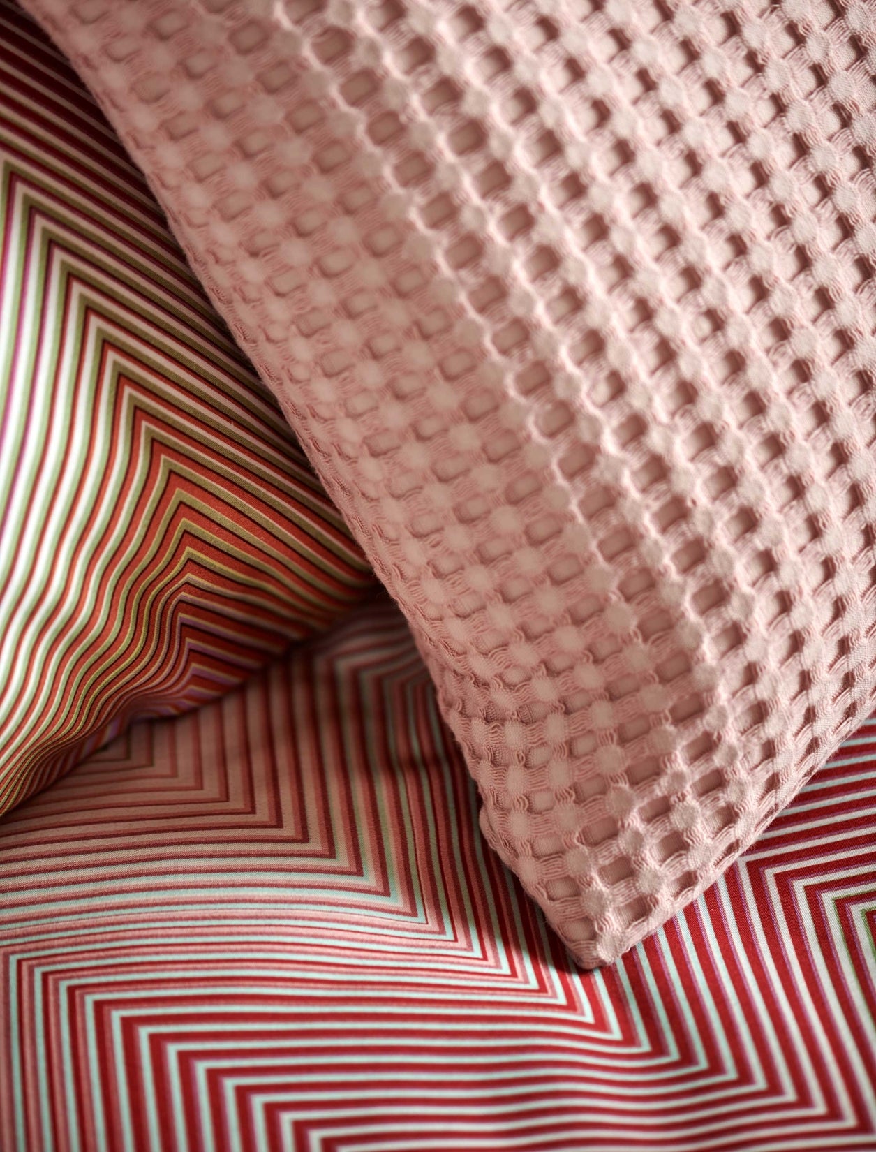 detail shot van een dekbedovertrek met zigzag print in roze en groene tinten en een sierkussen met wafelprint in een roze kleur