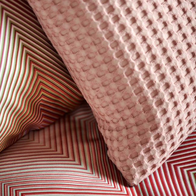 detail shot van een dekbedovertrek met zigzag print in roze en groene tinten en een sierkussen met wafelprint in een roze kleur