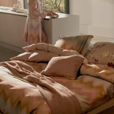 Vrouw die in een keuken staat en een bed met een dekbedovertrek in mooie diepe paarse en roze kleuren