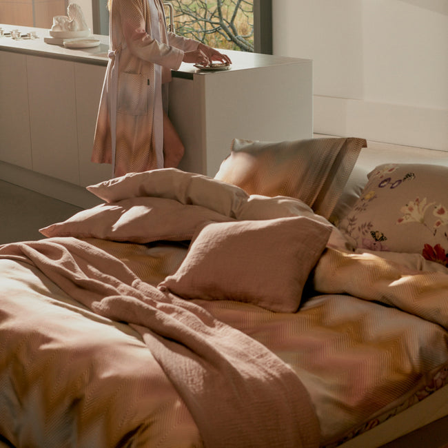 Vrouw die in een keuken staat en een bed met een dekbedovertrek in mooie diepe paarse en roze kleuren