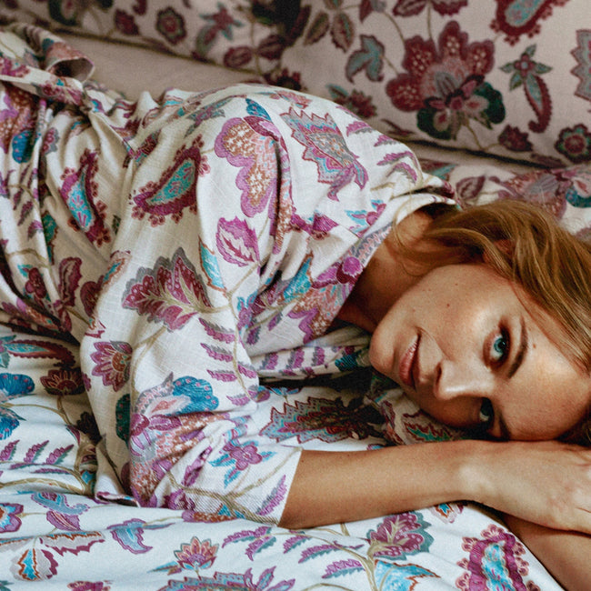 Een vrouw die op een bed ligt met een badjas aan met paisley pirnt in paarse en blauwe kleuren met een dekbedovertrek in dezelfde print