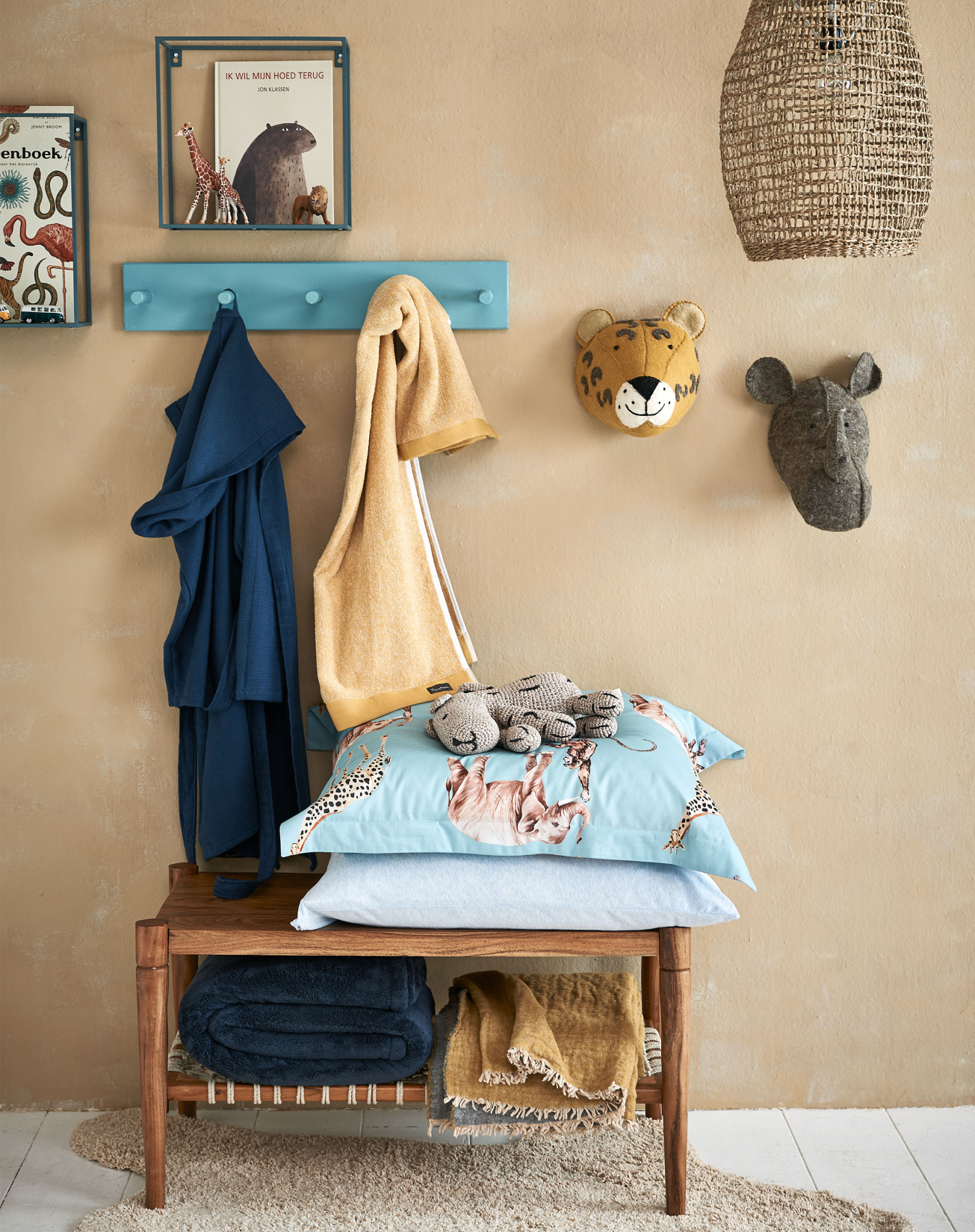 een kinderkamer met een blauwe kapstok waar een blauwe kinderbadjas aan hangt en een stoffen tijger en neushoorn die aan de muur hangen.